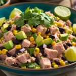 A vibrant bowl of Mexican Tuna Salad with tuna, avocado, black beans, corn, and cilantro, garnished with fresh lime wedges